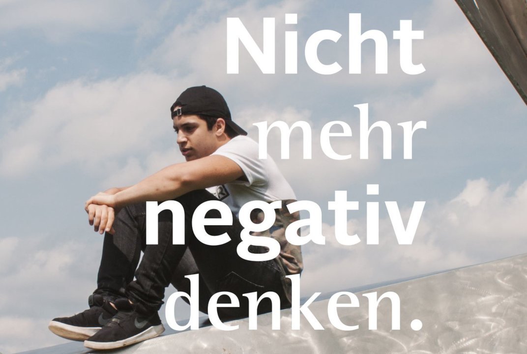 Junger Mann sitzt auf einer Rampe, auf dem Bild ein Schriftzug "Nicht mehr negativ denken"